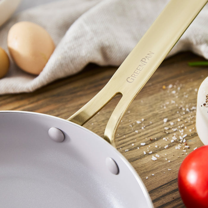 Stainless steel frypan set with visible handles on wood, eggs, a tomato, and salt nearby.