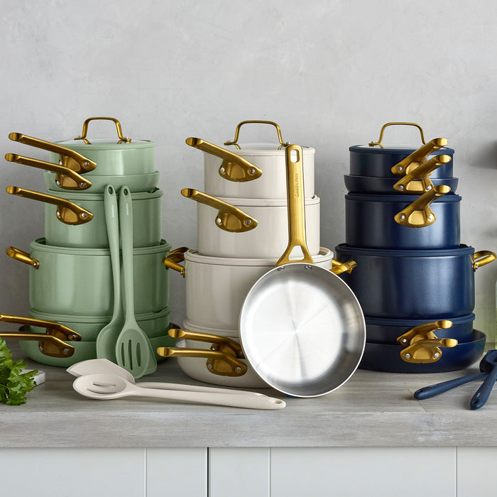 Set of pots, pans, and kitchen utensils with gold handles on a gray surface.