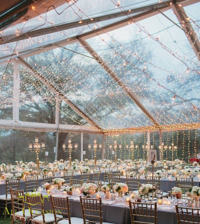 Bistro Lighting Rental 37.5ft white string lights illuminating an elegant banquet tent setting for a wedding.