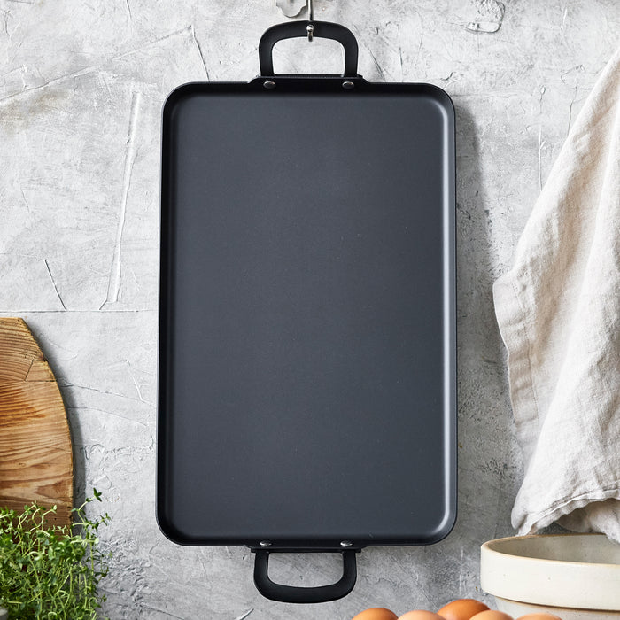 Carbon steel double burner griddle with side handles on a concrete countertop.