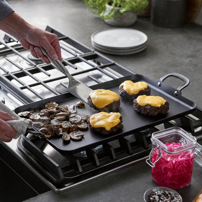 Carbon steel double burner griddle cooking cheeseburgers and mushrooms, with pickled onions on the side.