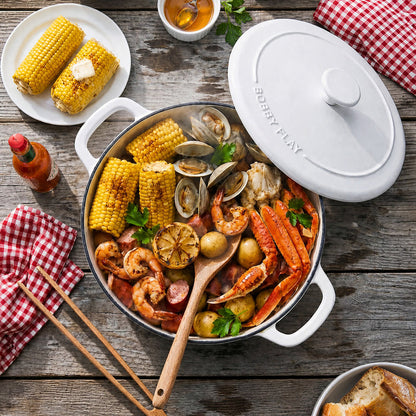 Ivory ceramic Dutch oven filled with seafood boil, placed on a rustic table next to bread.