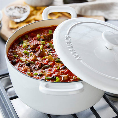 Ivory Dutch oven with lid partially on, filled with chili and veggies, resting on a stovetop. 5.5-quart size visible.