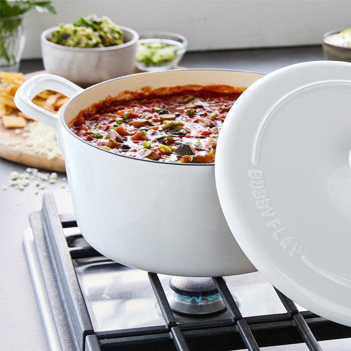Ivory Dutch oven with chili simmering inside, beans and veggies visible, lid partially open on the stove.