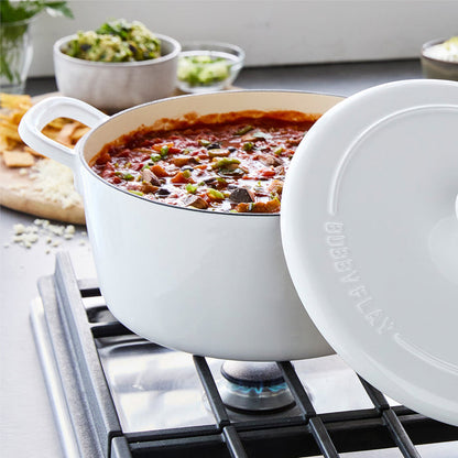 Ivory Dutch oven with chili simmering inside, beans and veggies visible, lid partially open on the stove.