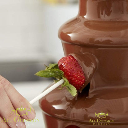 Chocolate fountain with 2 bags of chocolate with a strawberry being dipped in warm chocolate.