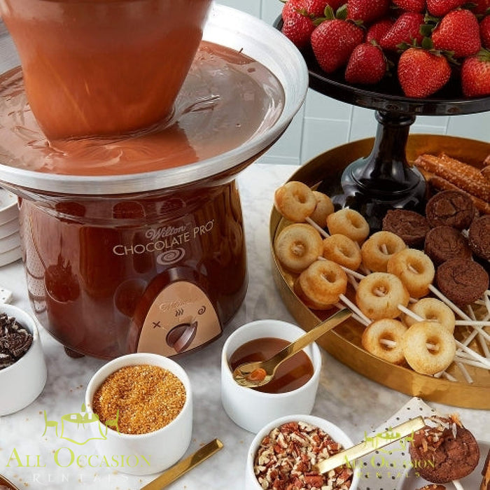 Chocolate fountain with 2 bags of chocolate showcasing melted chocolate, strawberries, and assorted dippables.