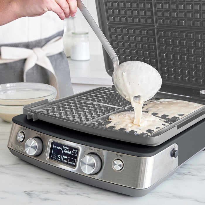 Batter being poured onto a graphite Elite Ceramic 4-square waffle maker on a kitchen counter.