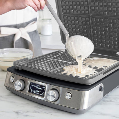 Batter being poured onto a graphite Elite Ceramic 4-square waffle maker on a kitchen counter.