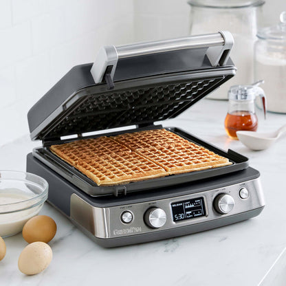 Graphite ceramic 4-square waffle maker on a white kitchen counter, waffles visible inside.