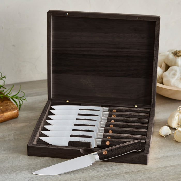 8-piece steak knife set with dark wood handles arranged in an open box on a kitchen counter.