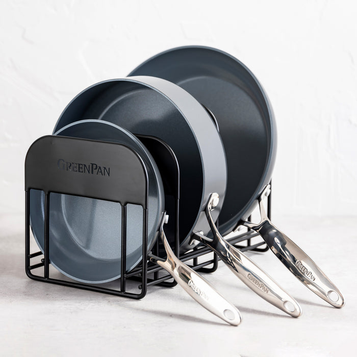 Three frying pans with forward-facing handles in a GreenPan rack on a white surface.