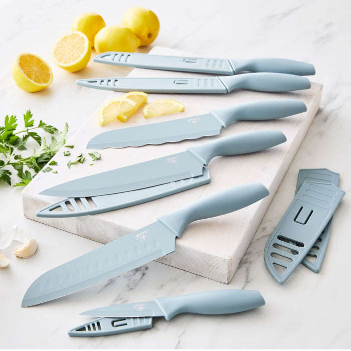 Blue six-piece cutlery set on a white cutting board with lemons, parsley, and garlic nearby.