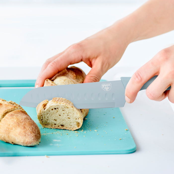 Blue GreenLife 6-piece cutlery set slicing a baguette on a blue cutting board.