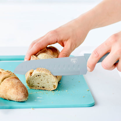 Blue GreenLife 6-piece cutlery set slicing a baguette on a blue cutting board.