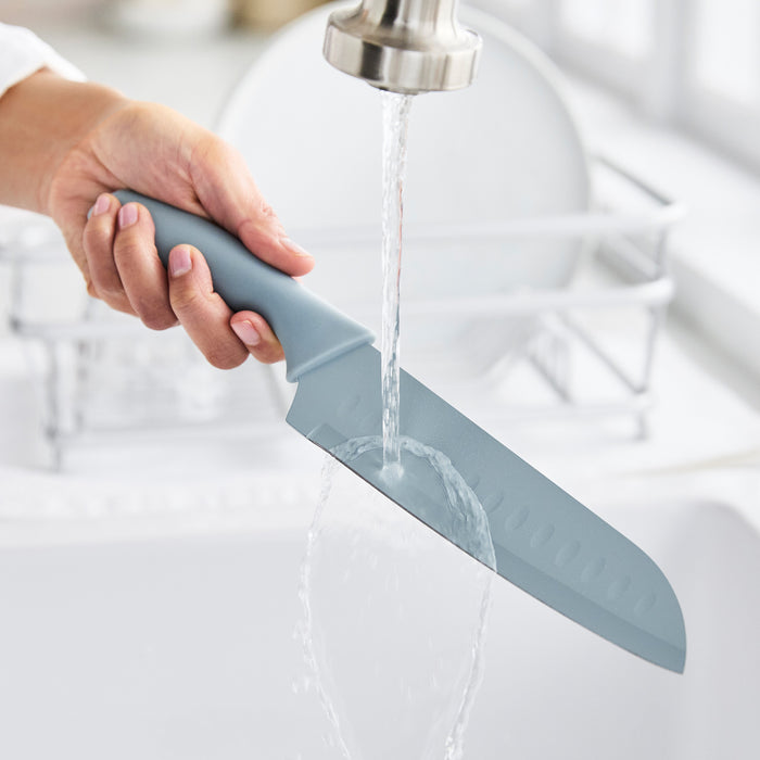 Hand washing a blue GreenLife cutlery knife under tap water in a sink, with other dishes nearby.