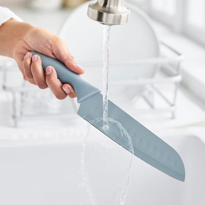 Hand washing a blue GreenLife cutlery knife under tap water in a sink, with other dishes nearby.