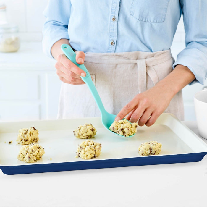 Cookie dough being placed onto a navy ceramic nonstick baking sheet with a spatula.