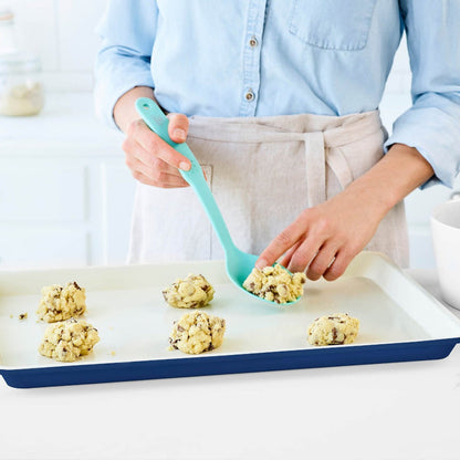 Cookie dough being placed onto a navy ceramic nonstick baking sheet with a spatula.