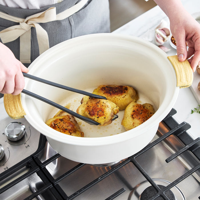 Person cooking chicken in a pot on a stove using tongs