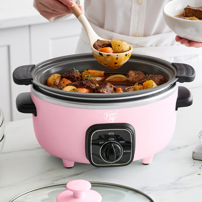 Pink slow cooker with beef and vegetable stew, being served with a ladle.