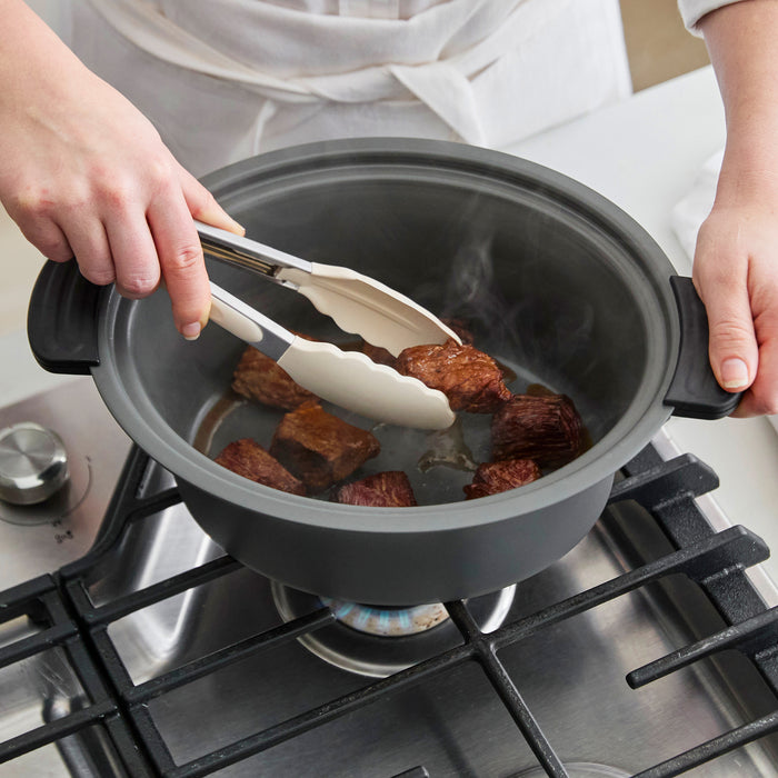 Person using tongs to handle food in a pot on a stove