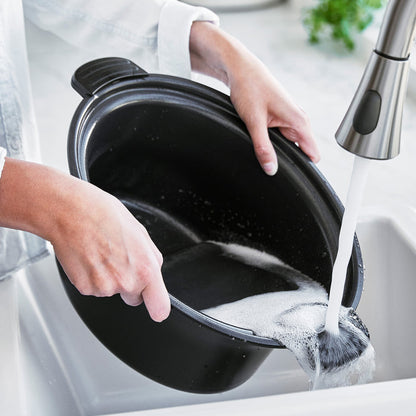 Person washing a pot under running water in a kitchen sink.