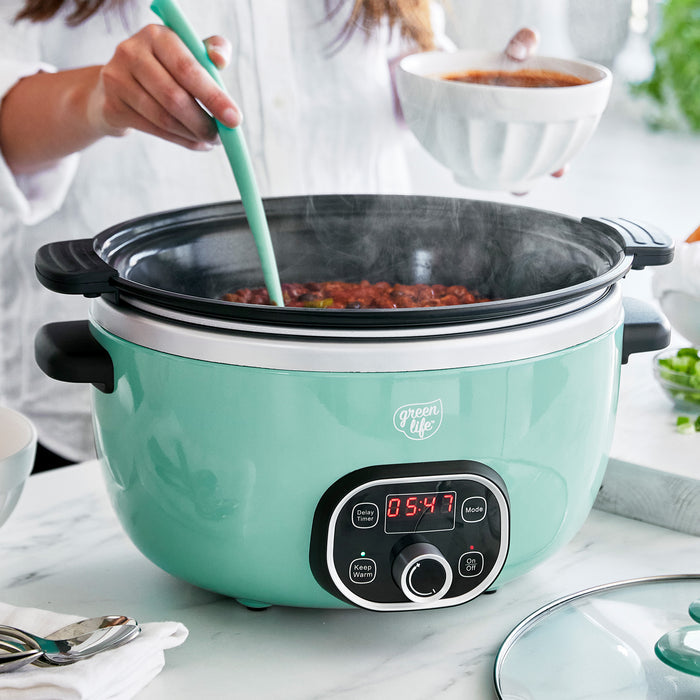 Turquoise slow cooker with a digital display on a kitchen counter, being used to cook food.