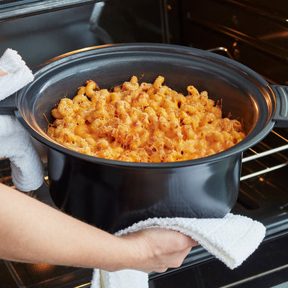 Person holding a pot with macaroni and cheese above an open oven.
