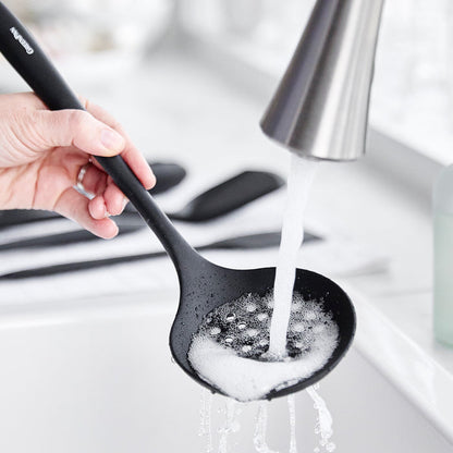 Black ladle and pot being washed with soap in a white sink under a kitchen faucet.