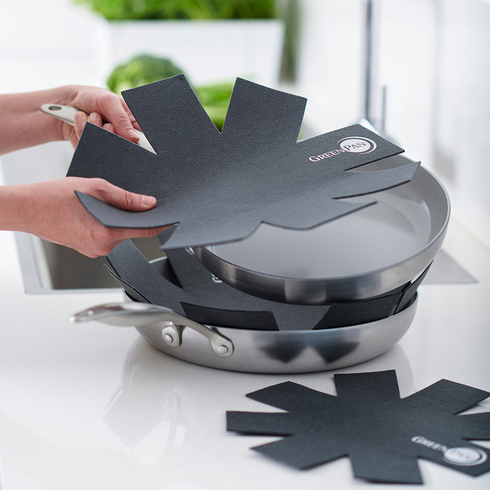 GreenPan felt pan protector placed between two stacked skillets on a kitchen counter near a sink.