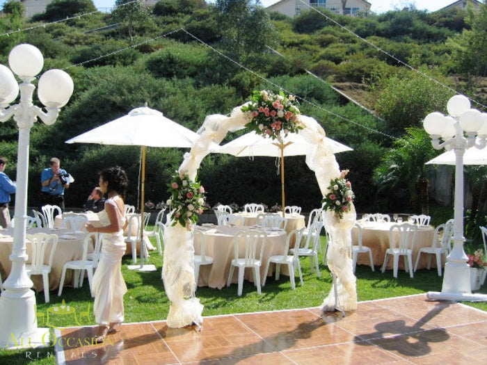 Elegant white iron arch at an outdoor wedding setup with banquet tables and chairs, ideal for event rentals in Corona.
