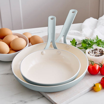 Set of frypans with handles on a kitchen counter with eggs and vegetables.