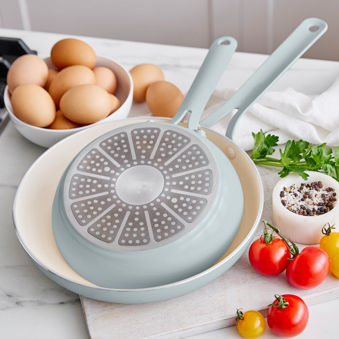 Light blue frying pan with a unique design on a kitchen counter with eggs and vegetables.