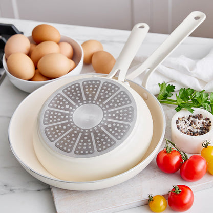 White frying pans on a kitchen counter with eggs and vegetables.