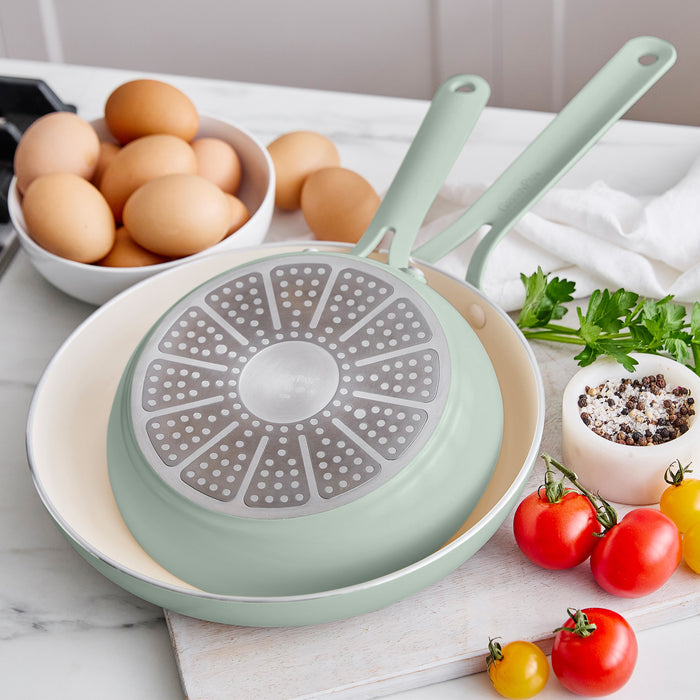 Green frying pan with a unique design on a kitchen counter with eggs and vegetables.