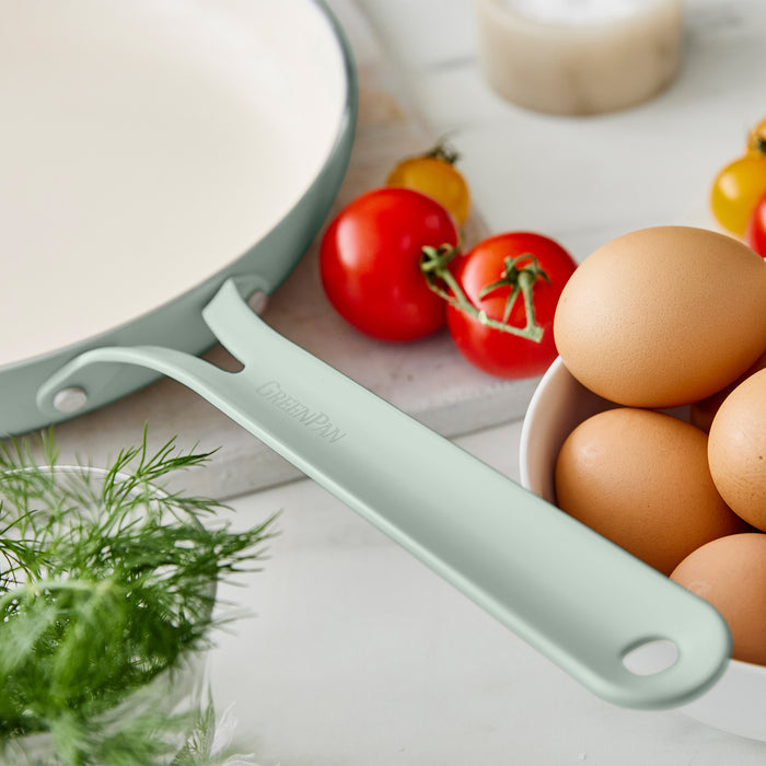 Green frypan on a white surface with tomatoes and eggs