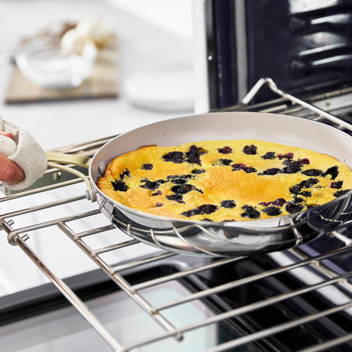Blueberry clafoutis in a stainless steel Nova Gallery frypan being taken out of the oven by a person.