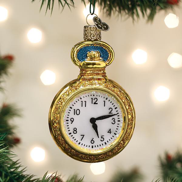 A gold pocket watch ornament showing the time as 5:00 hangs on a Christmas tree with blurred white lights in the background.