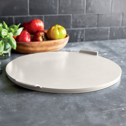 Taupe round pizza pan on a gray counter with tomatoes and basil nearby.