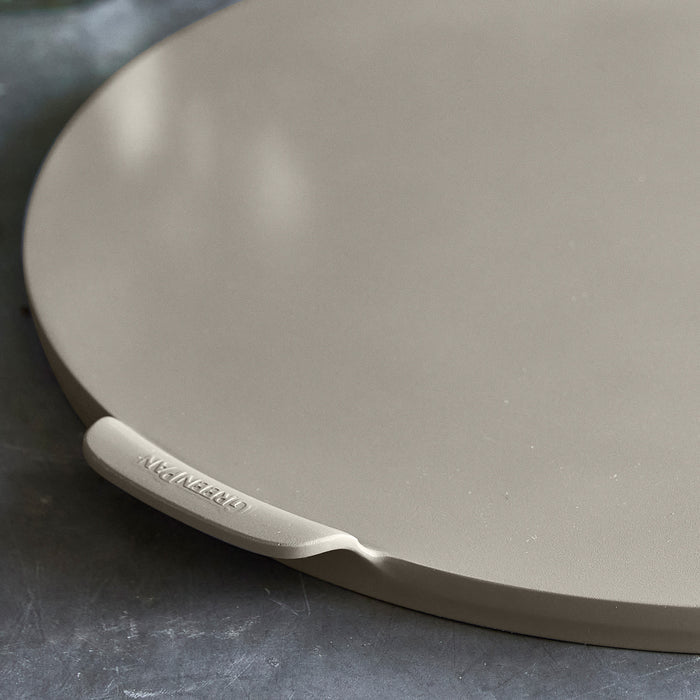 Taupe ceramic 16.5 round pizza baking pan with nonstick coating on a dark countertop.
