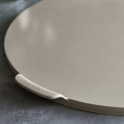 Taupe ceramic 16.5 round pizza baking pan with nonstick coating on a dark countertop.