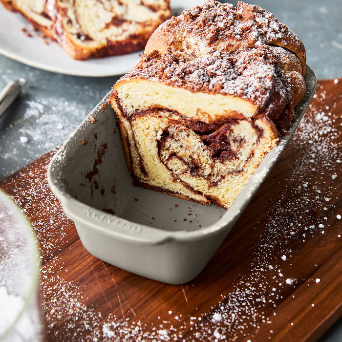 Taupe ceramic nonstick 5-piece bakeware set with sliced chocolate swirl bread dusted with powdered sugar.