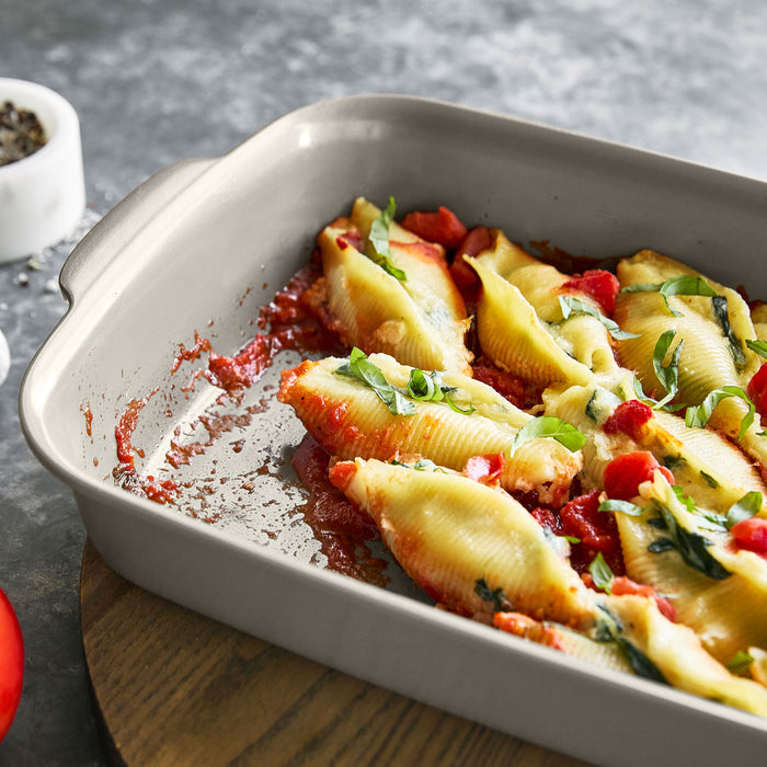 Partially eaten stuffed pasta shells with sauce in a white ceramic 13x9 baking dish.
