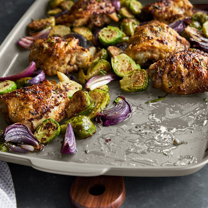 Roast chicken, brussels sprouts, and onions on a white ceramic half sheet pan with nonstick surface.