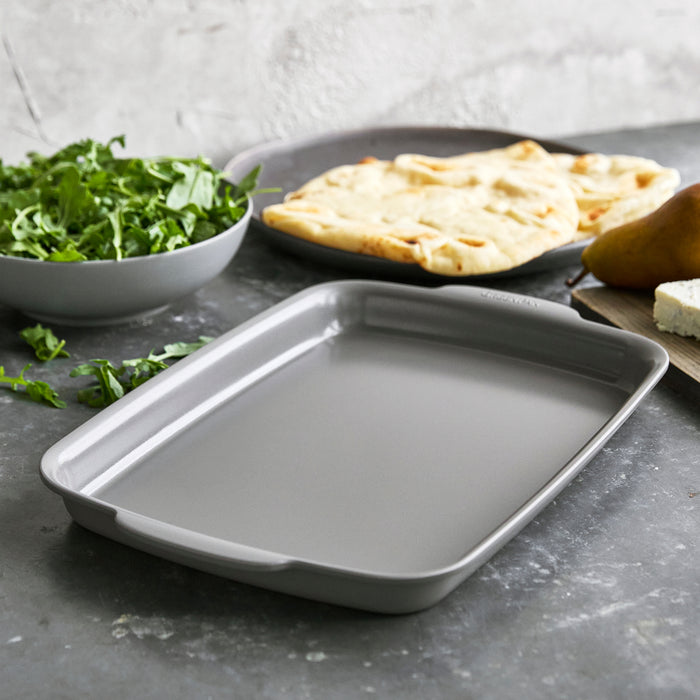 Gray ceramic nonstick 2-piece sheet pan set on counter, one pan topped with flatbread, arugula, pear, and cheese.