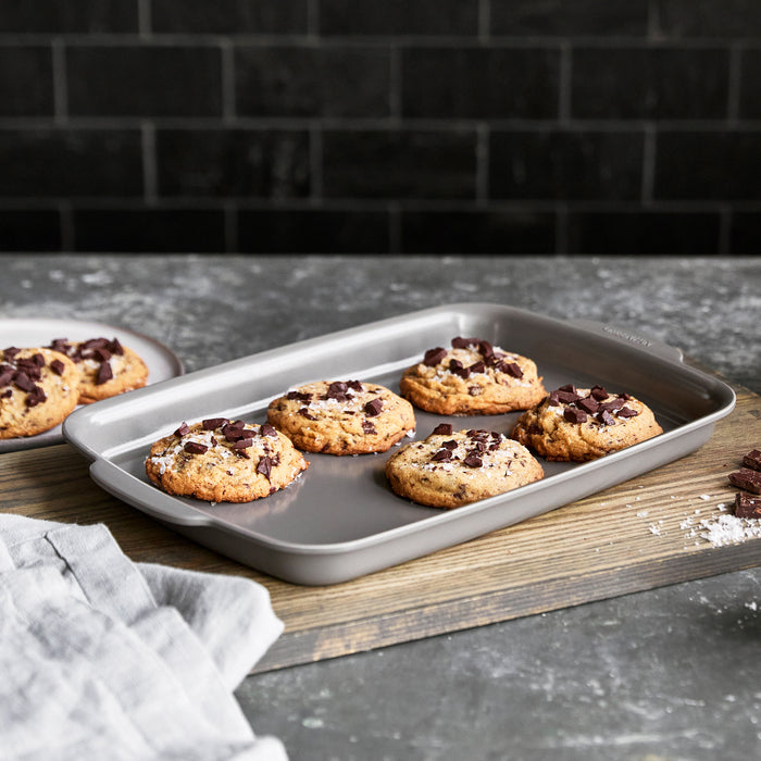 Ceramic nonstick quarter sheet pan with six cookies on a gray counter, next to a plate and napkin.