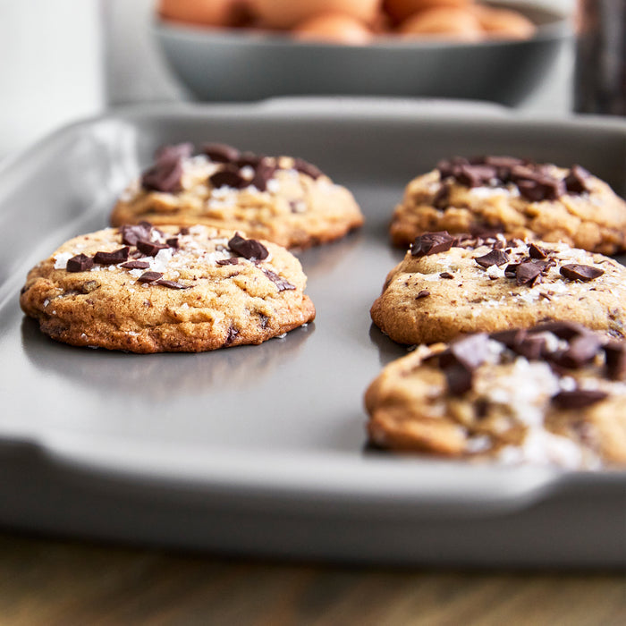 Four chocolate chip cookies on a ceramic nonstick quarter sheet pan set, topped with sea salt.