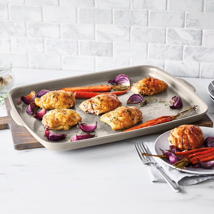 Roasted chicken thighs, carrots, and onions on a ceramic nonstick sheet pan set with pieces of the set shown nearby.