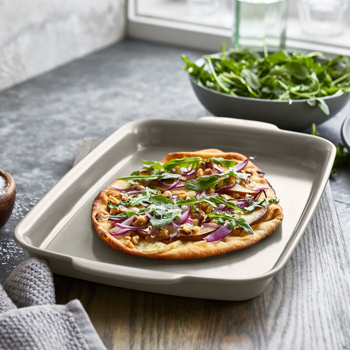 Flatbread pizza topped with onions, arugula, and walnuts on a ceramic nonstick 13x9 sheet pan.